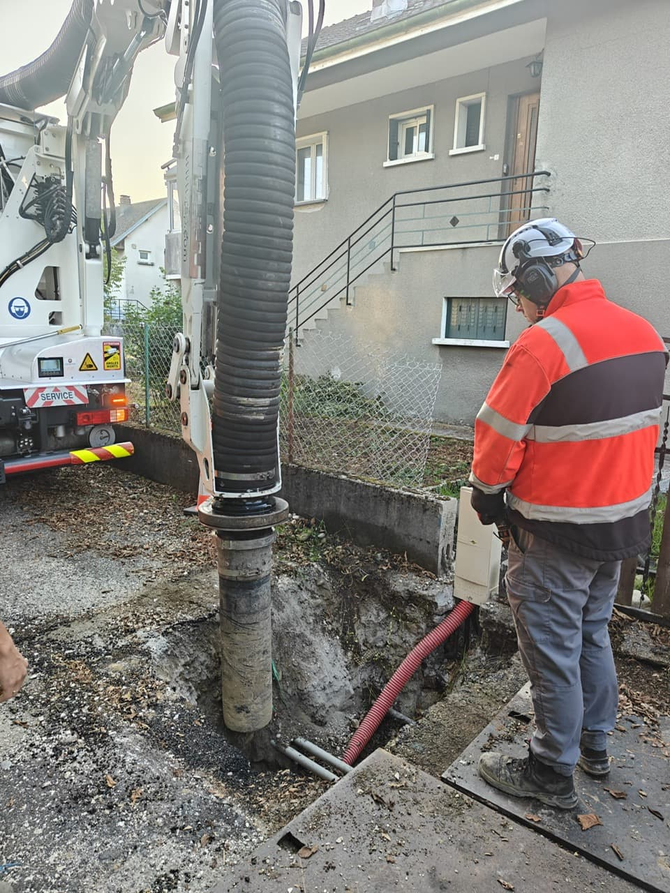 Opérateur AIX TP pilotant à distance l’aspiration au-dessus d’une fouille où apparaissent une gaine rouge et des fourreaux