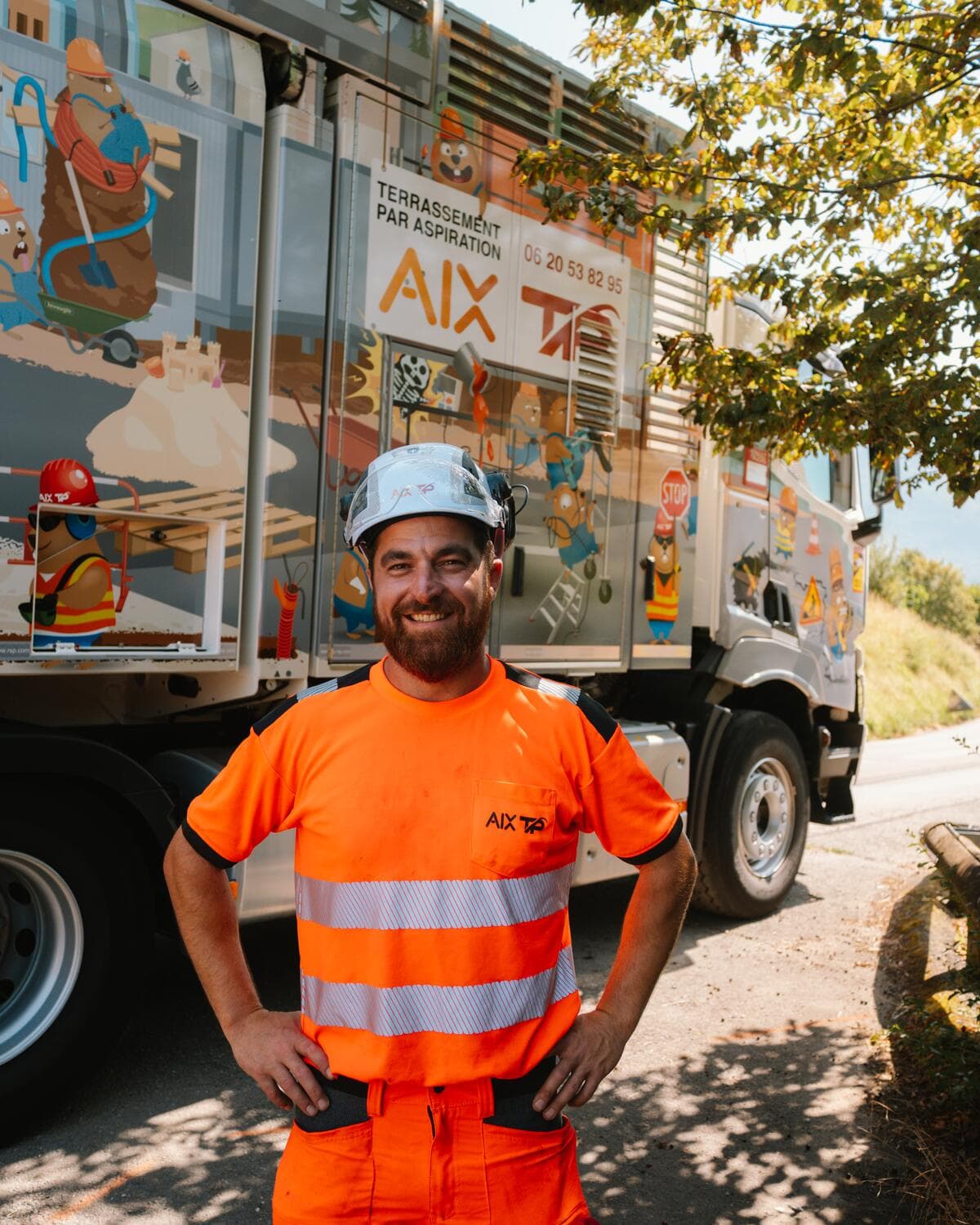 Opérateur AIX TP souriant, casque de chantier sur la tête, devant un camion aspirateur habillé de la fresque de marmottes