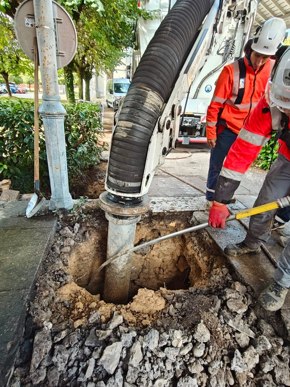 Deux opérateurs AIX TP dégageant une fouille, sous le flexible d’aspiration, sur un trottoir