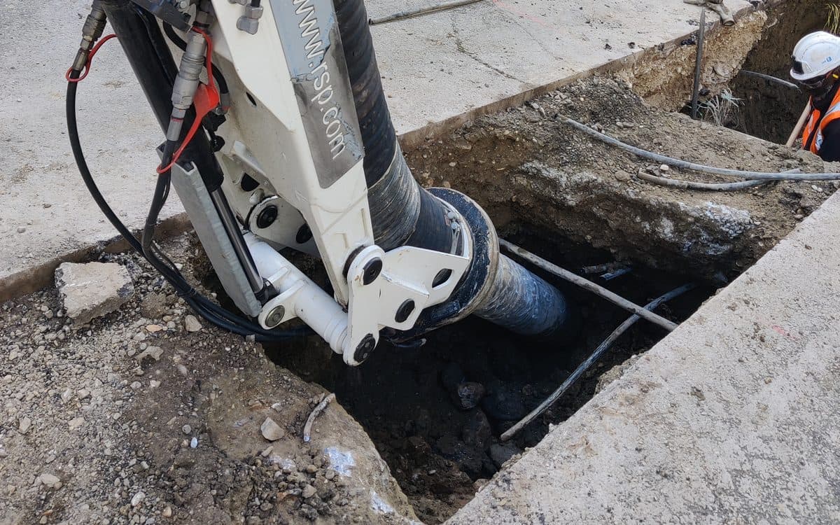 Tête d'aspiration engagée dans une fouille étroite entre deux bordures béton