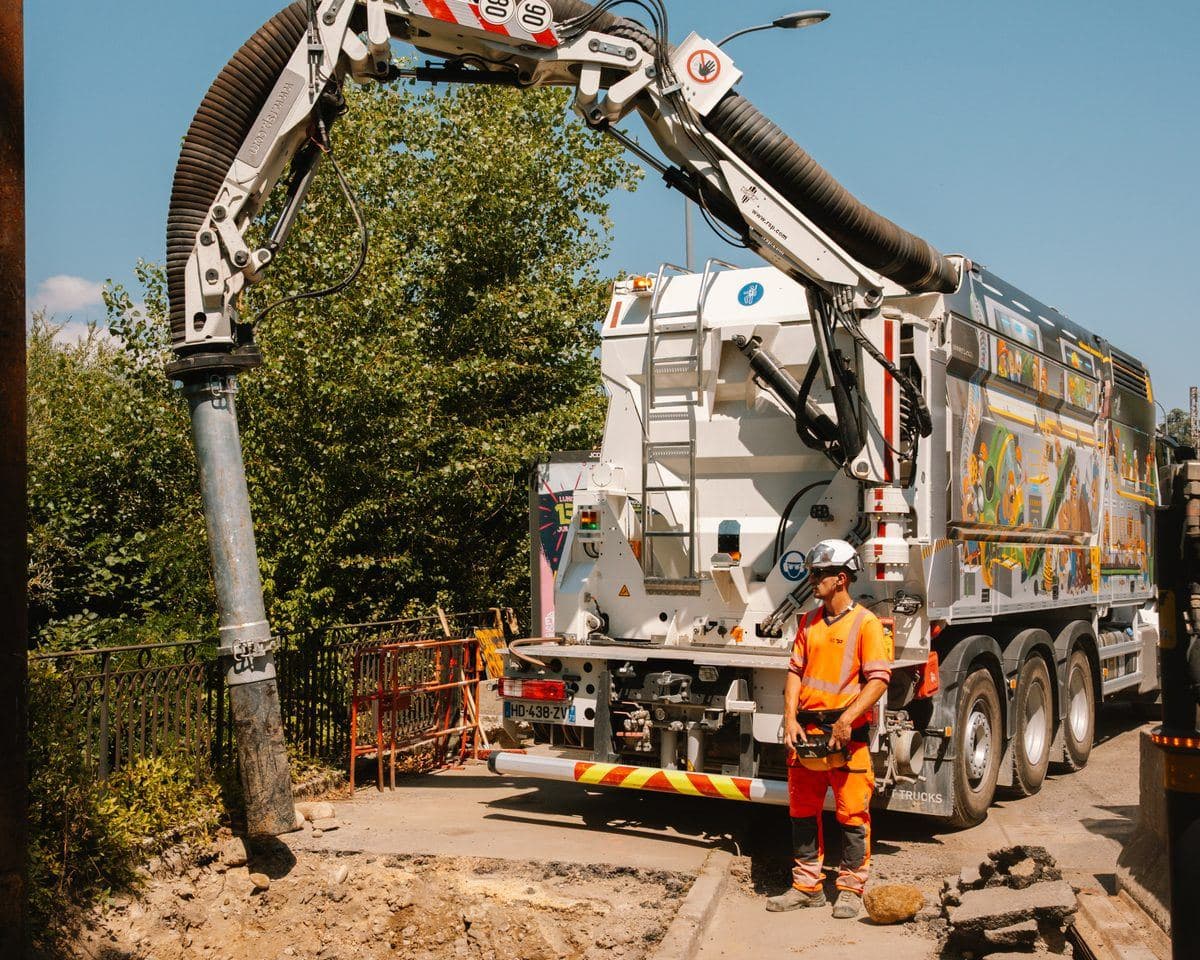 Camion excavateur aspirateur AIX TP en action, bras d'aspiration déployé en arc de cercle au-dessus d'une fouille