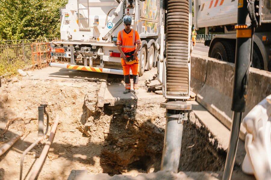 Tube d'aspiration engagé dans une fouille étroite entre deux bordures